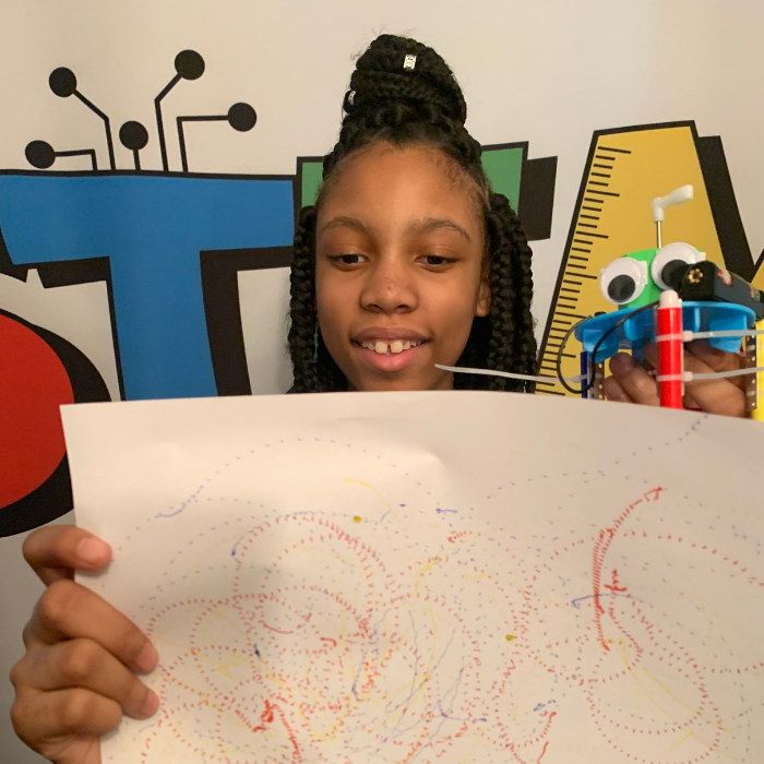 Alaina Davis showcasing the doodle artwork created by the plastic Graffiti Robot, highlighting its automated drawing capabilities.