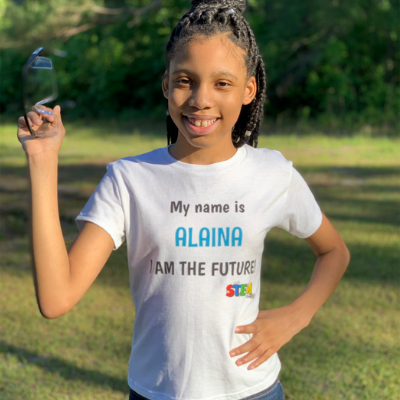 STEM Powered Kits Co-Owner and CEO Alaina Davis smiling and holding safety glasses while wearing a STEM T-shirt that reads 'My Name is Alaina, I Am the Future,' motivating future STEM leaders.