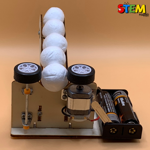 Front view of the assembled Ball Pitching Machine STEM Kit, featuring a motorized pitching mechanism and plastic balls lined up for STEM learning.