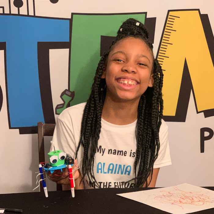 Alaina Davis, Co-Owner and CEO of STEM Powered Kits, proudly holding the plastic version of the Graffiti Robot while smiling during a STEM activity.