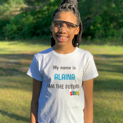 Alaina Davis, Co-Owner and CEO of STEM Powered Kits, wearing a STEM T-shirt with her name and the slogan 'I Am the Future,' inspiring young innovators.